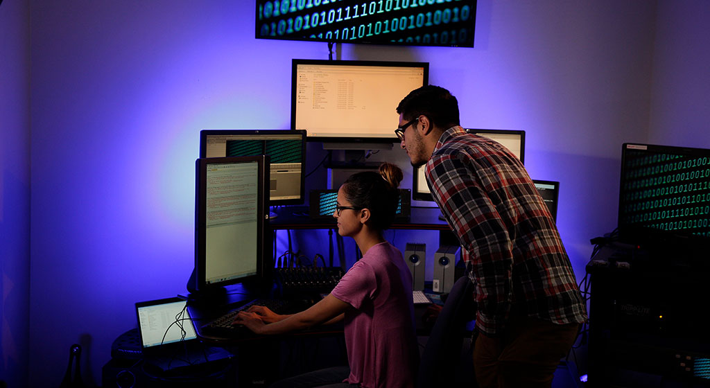 Man assisting woman sitting at computer station