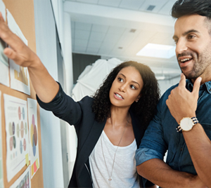 woman points at paper on a board while a man looks on