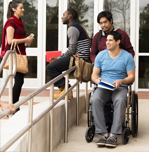 college students outside a campus building, one student in a wheel chair on a ramp