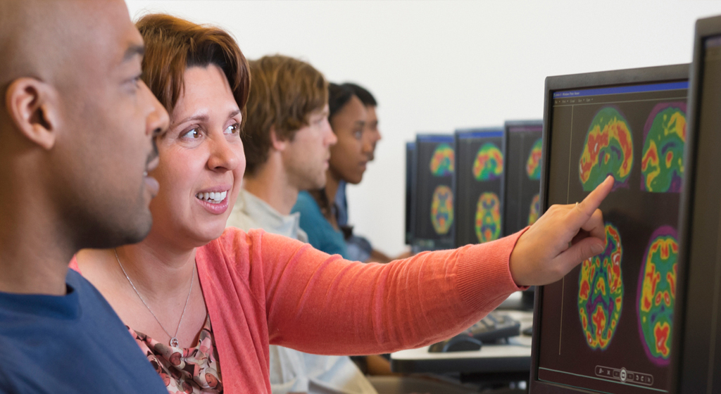 instructor points to a brain scan on a computer monitor while a male student looks on