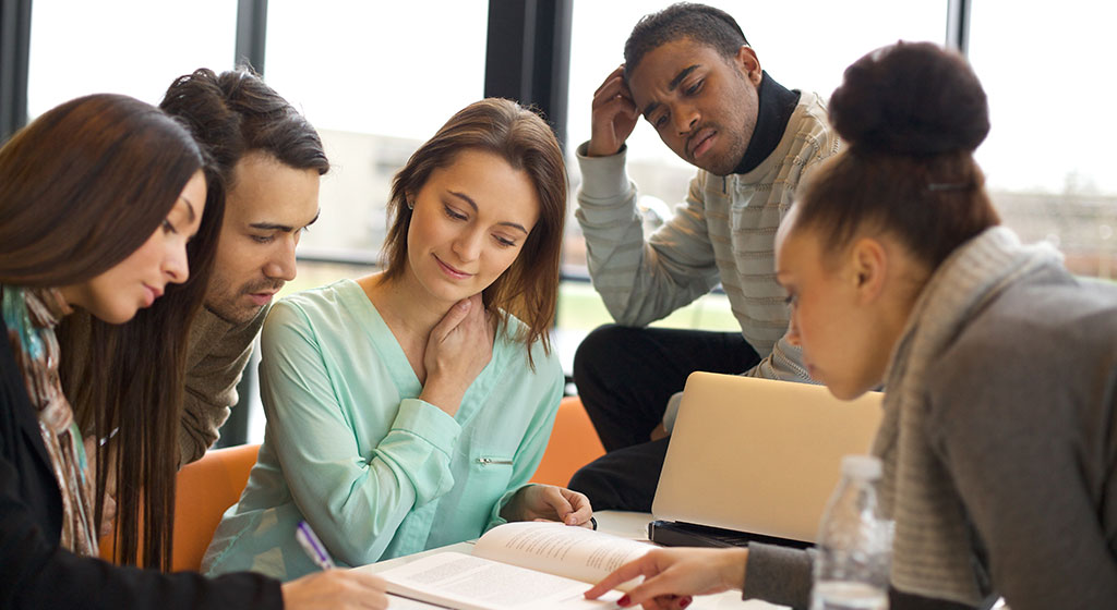 group of college students gathered around a text book