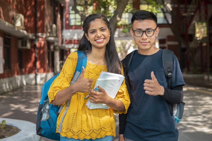 two students giving thumbs up in front of school