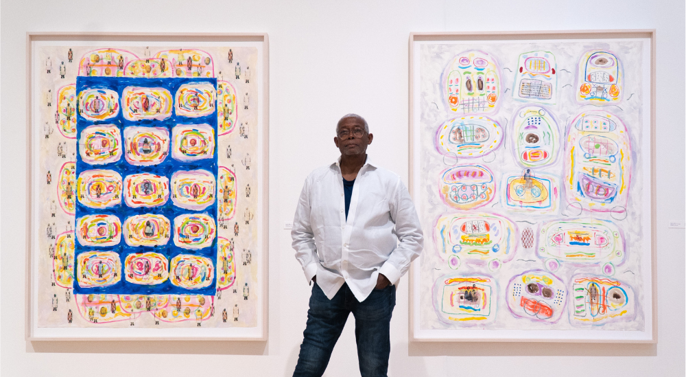 Floyd Newsum standing in front of 2 of his art pieces