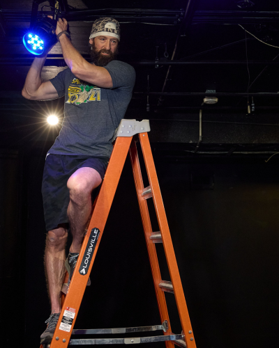 Luke Fedell stands on a ladder while holding a theatre light in the university of houston-downtown's O'Kane Theatre