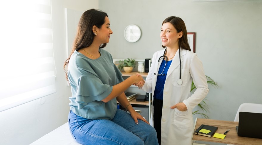 Female young adult sitting on medical table shaking hands with female doctor.