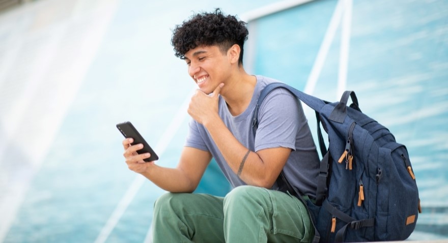 Male young adult sitting down smiling while looking at phone.