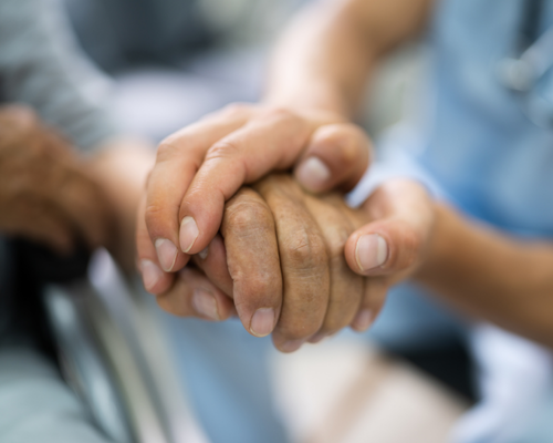 A nurse holds an older adult's hand 