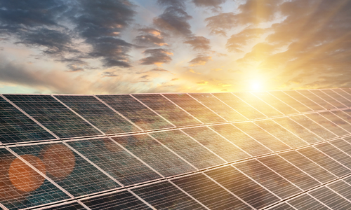 Solar panels glimmer in the sunlight as the sun sets. Clouds in the sky.