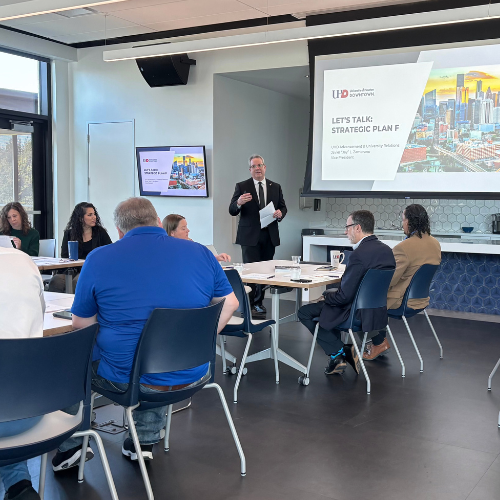 Faculty and staff sit at small groups while Jay Zambrano speaks at a strategic plan seminar on plan F