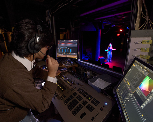 A theatre student operates a sound and lighting board while an actress is on the stage at the o'kane theatre at the university of houston-downtown