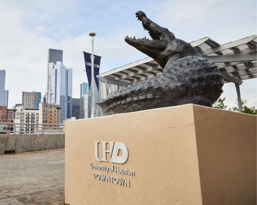 an alligator statue on the university of houston-downtown's south deck. the downtown houston skyline is in the background.